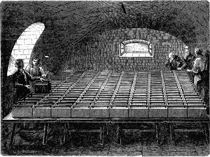 Engraving of a vaulted cellar filled with long rows of battery troughs, with several men standing at one end.